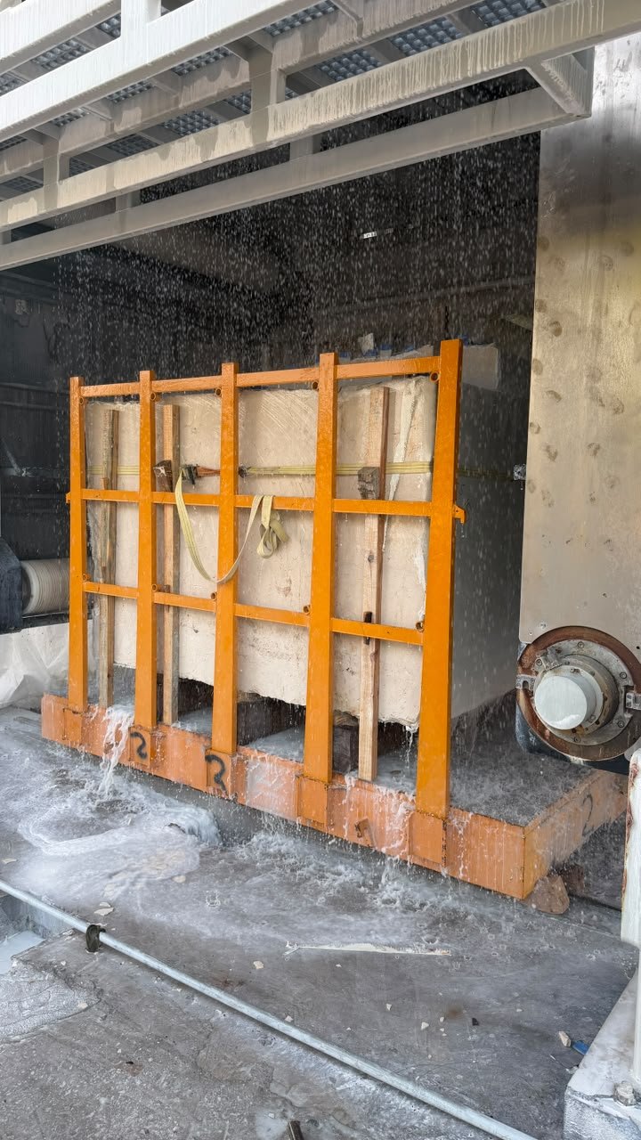Thin-wire marble cutting machine processing a stone block under water spray
